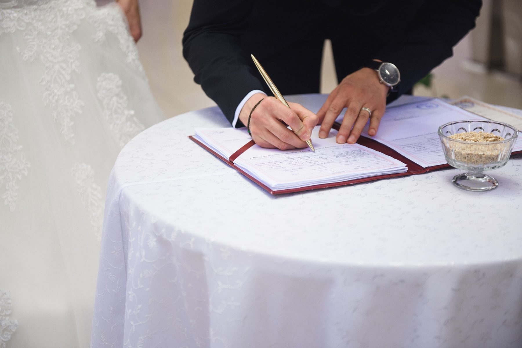 Groom signing a wedding venue contract at a white draped table