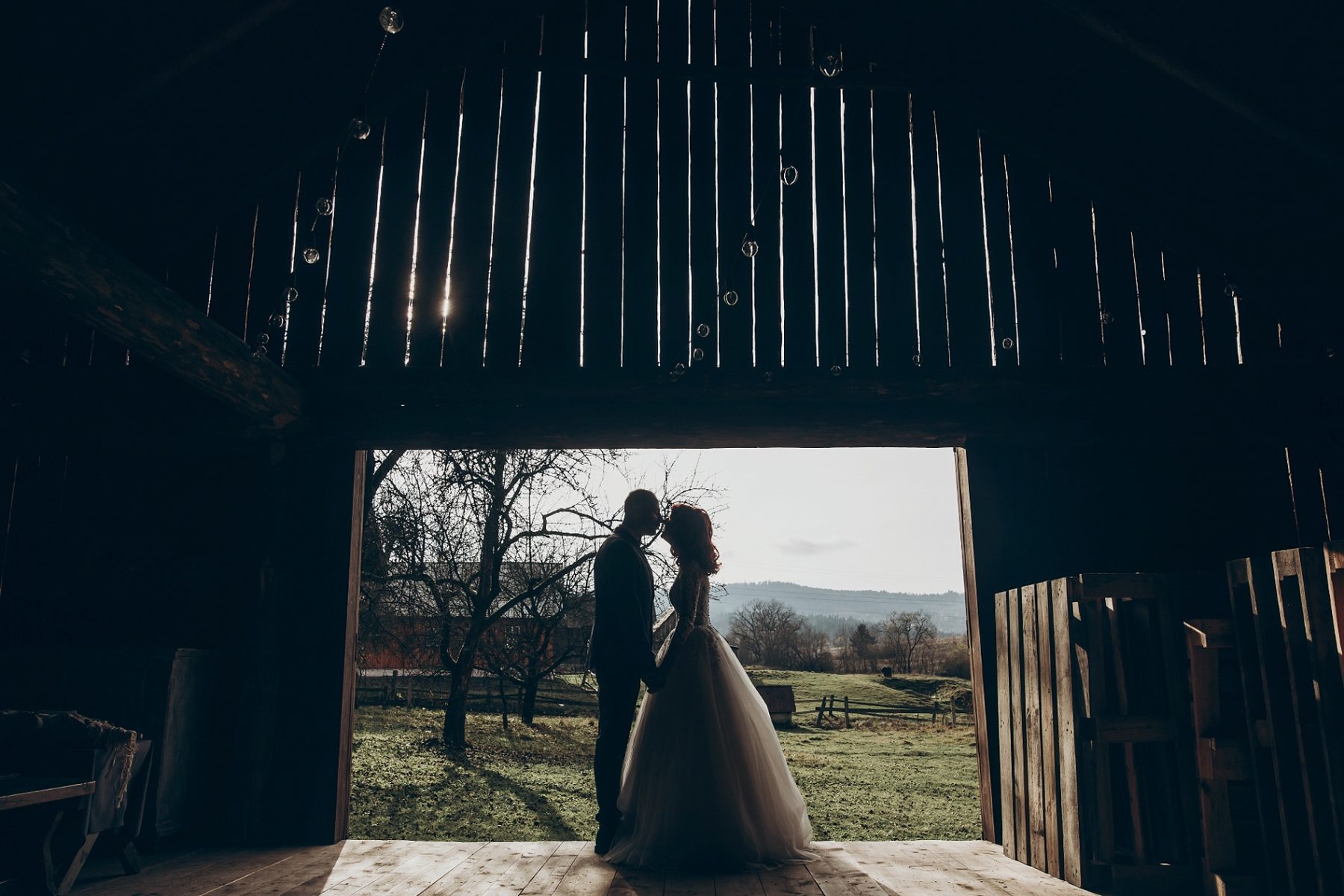 Bride and groom silhouetted in an open barn doorway at sunset