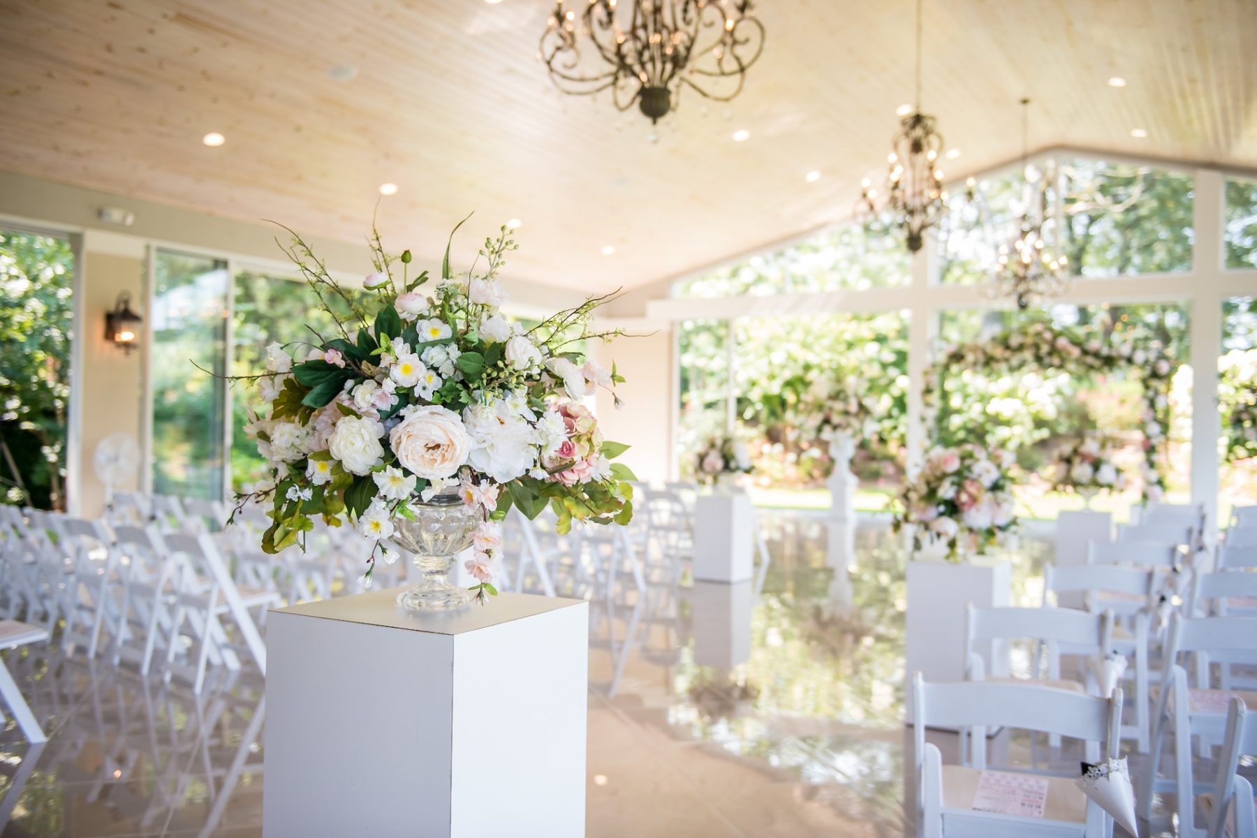 Bright garden wedding ceremony aisle with chandeliers and floral urns