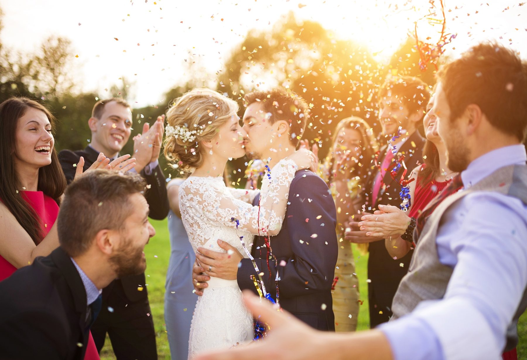 Bride and groom kissing under a shower of confetti with cheering guests at golden hour