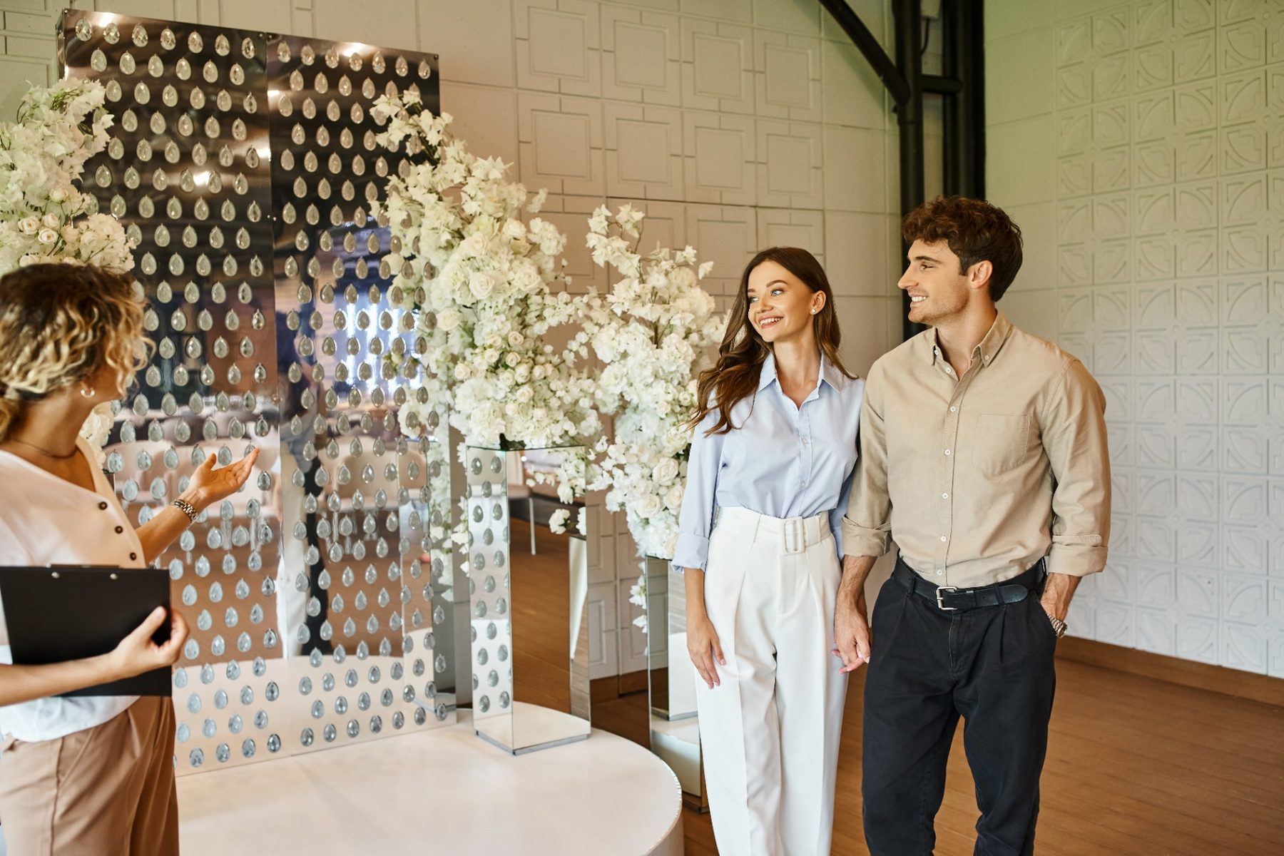 Venue owner showing white floral decor to a smiling engaged couple during a tour