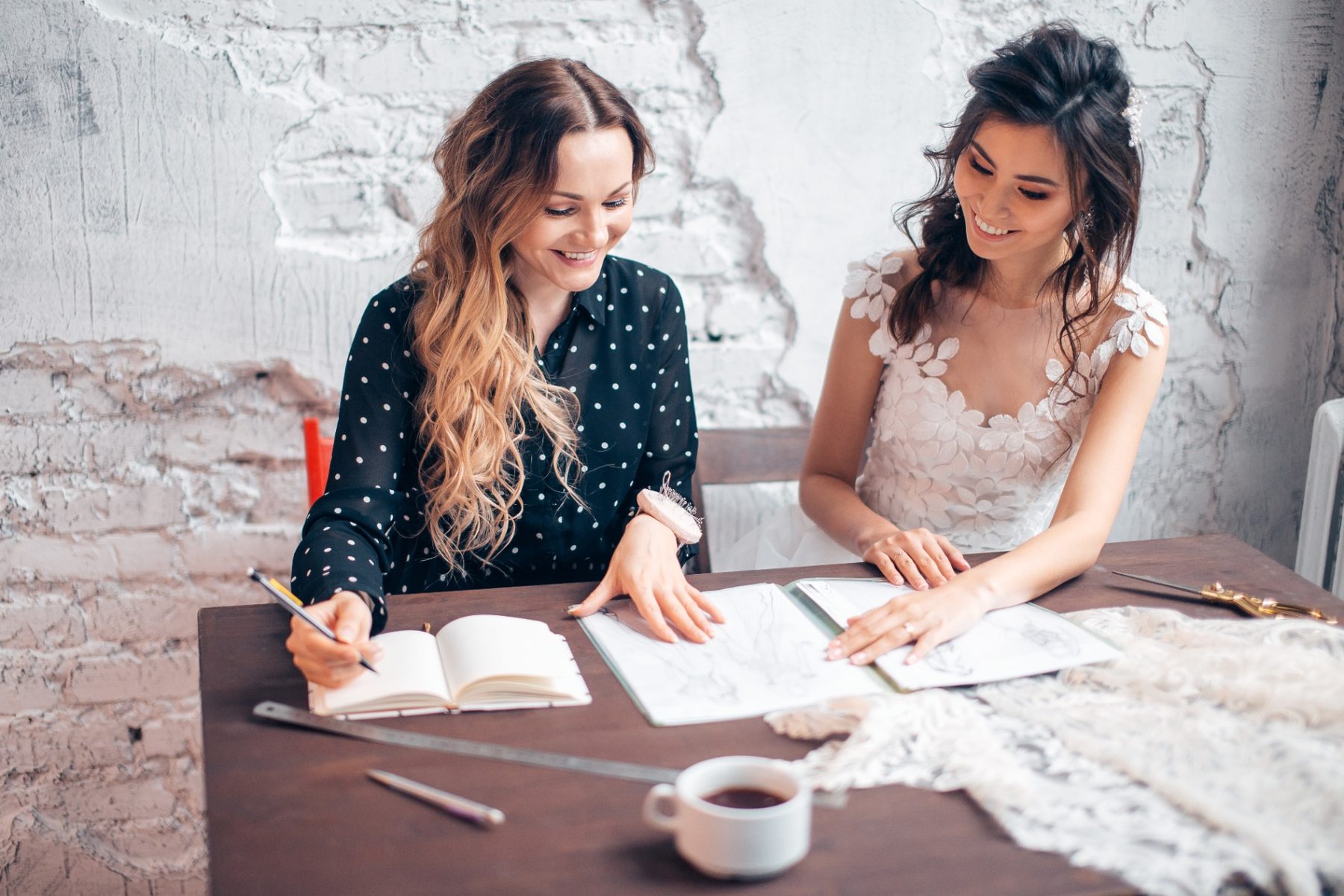 Wedding coordinator planning ceremony details with a bride at a wooden table
