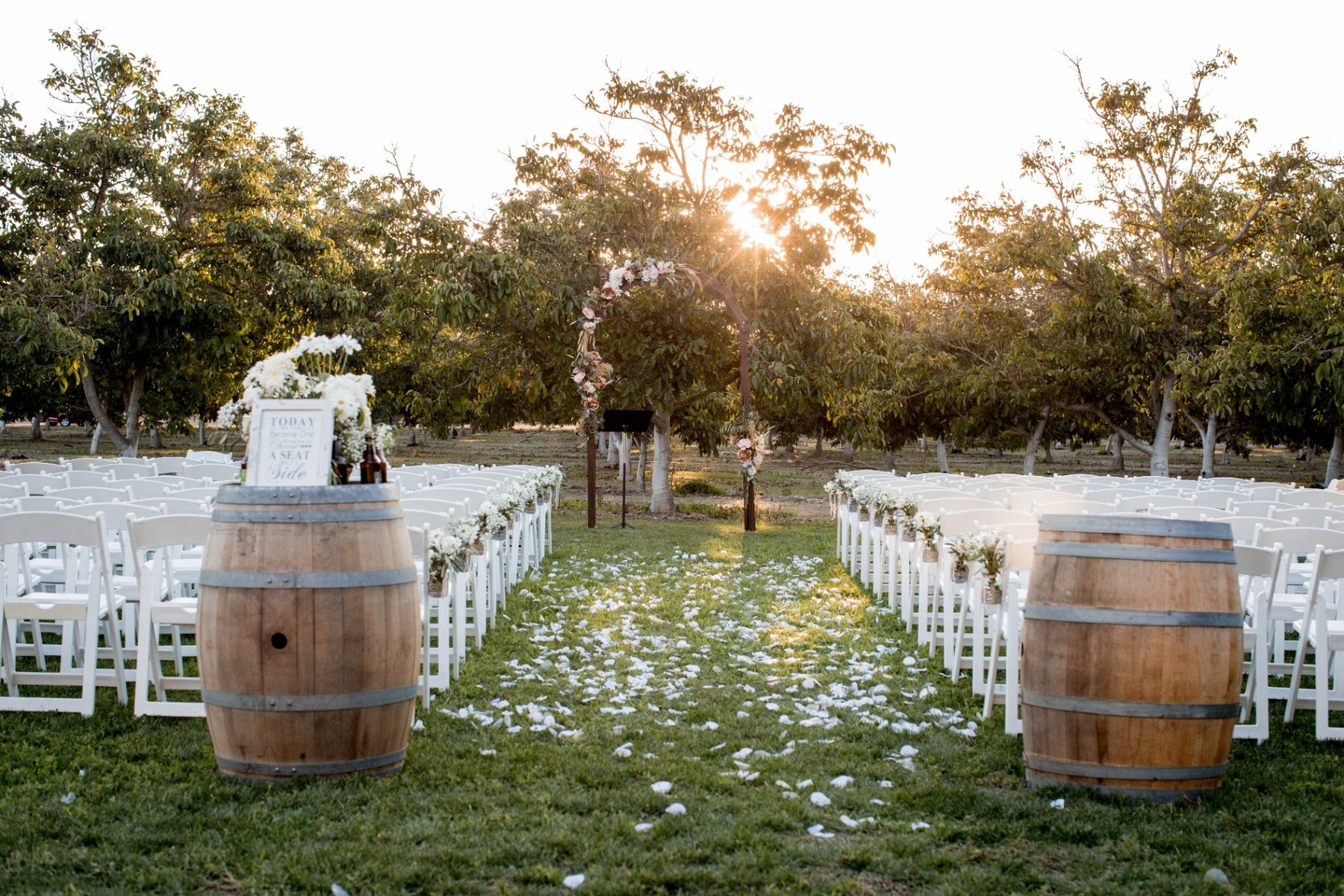 Rustic outdoor wedding ceremony aisle with wine barrels at sunset